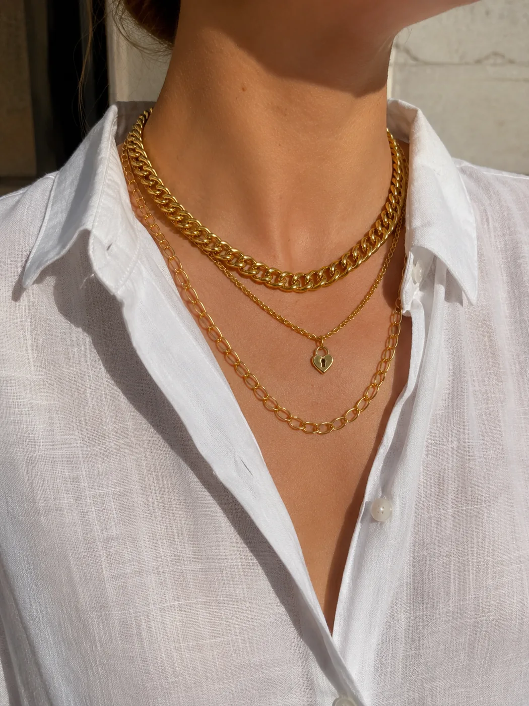 Layered gold chains and a heart padlock pendant worn with a white shirt